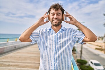 Young hispanic man smiling happy listening to music at the promenade.