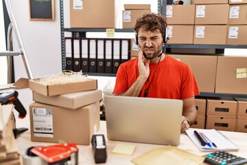 Young hispanic call center agent man working at warehouse touching mouth with hand with painful expression because of toothache or dental illness on teeth. dentist concept.