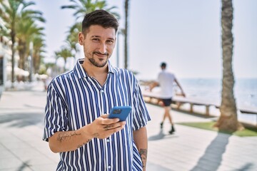 Young handsome man using smartphone by the sea