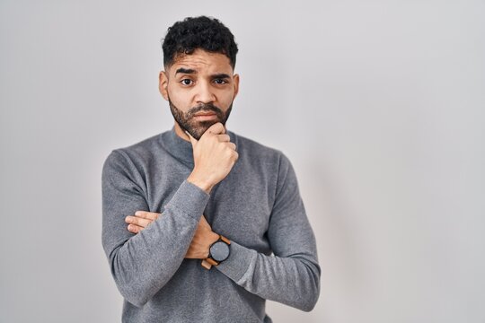 Hispanic man with beard standing over white background thinking worried about a question, concerned and nervous with hand on chin