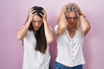 Mother and daughter standing together over pink background suffering from headache desperate and stressed because pain and migraine. hands on head.
