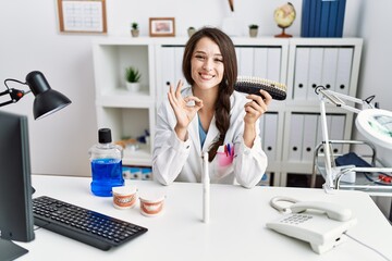 Young dentist woman comparing teeth whitening doing ok sign with fingers, smiling friendly gesturing excellent symbol