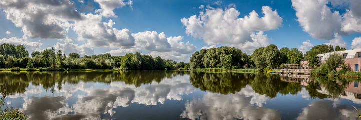 Fototapeta na wymiar Panorama photo of typical Dutch clouds above the water of Westerpark in Zoetermeer.