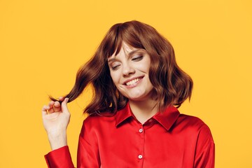 a pleasant, charming woman stands in a stylish red shirt on a yellow background and touches her hair with a cute smile. Horizontal photo with an empty space for inserting an advertising layout