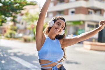 Young beautiful hispanic woman listening to music and dancing at street