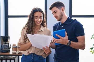 Young hispanic couple business workers using touchpad reading document at office