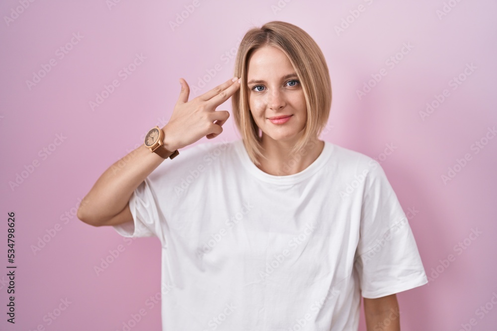 Sticker Young caucasian woman standing over pink background shooting and killing oneself pointing hand and fingers to head like gun, suicide gesture.