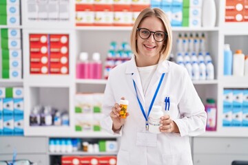 Young blonde woman pharmacist smiling confident holding pills bottles at pharmacy