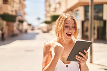 Young blonde woman smiling confident using touchpad at street