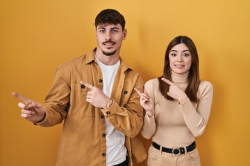 Young hispanic couple standing over yellow background pointing aside worried and nervous with both...