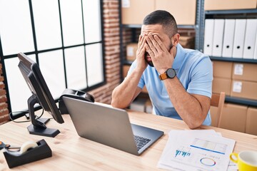 Naklejka premium Young latin man ecommerce business worker stressed using laptop at office
