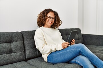 Middle age hispanic woman smiling confident using touchpad at home