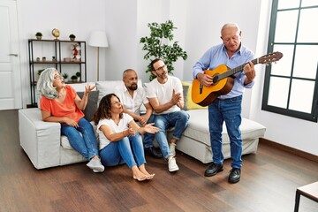 Group of middle age friends having party playing classical guitar sitting on the sofa at home.