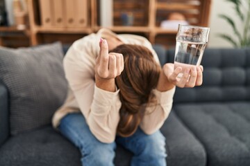 Young caucasian man patient stressed holding pill and glass of water at psychology clinic