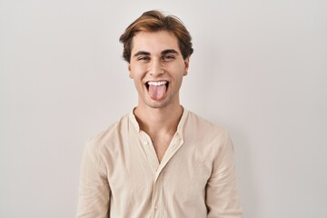 Young man standing over isolated background sticking tongue out happy with funny expression....