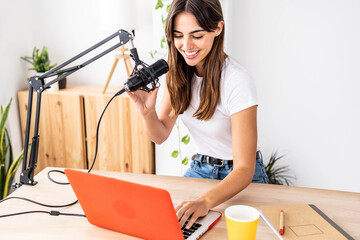 Professional female podcaster recording podcast on computer from home studio - Millennial...