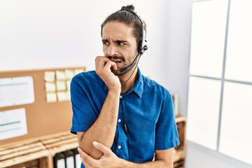 Young hispanic man with beard wearing call center agent headset at the office looking stressed and...