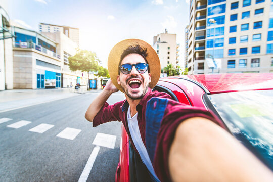 Young handsome man taking selfie picture in the car - Happy tourist driving a rental car on city street - Transportation, travel and vacations concept