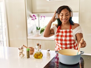 Hispanic brunette woman cooking wearing headphones at the kitchen