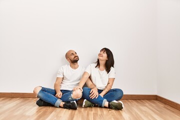 Fototapeta na wymiar Young hispanic couple smiling happy sitting on the floor at empty new home.