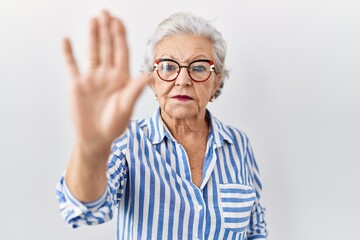 Senior woman with grey hair standing over white background doing stop sing with palm of the hand....