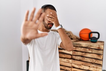 African american man listening to music using headphones at the gym covering eyes with hands and doing stop gesture with sad and fear expression. embarrassed and negative concept.