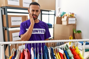African american man wearing volunteer t shirt at donations stand touching mouth with hand with...