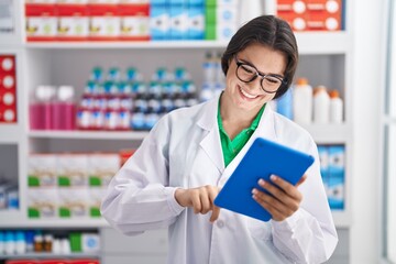 Young hispanic woman pharmacist smiling confident using touchpad at pharmacy
