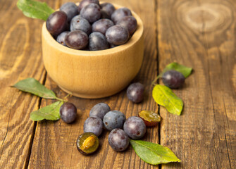 Blue plum in a bowl on a wooden table. Fruit background with copy space.