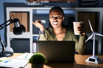 African woman working using computer laptop at night pointing aside worried and nervous with forefinger, concerned and surprised expression