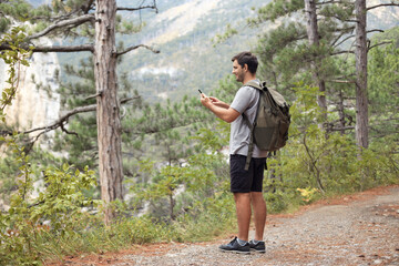 Full body tourist man with backpack in the mountain forest using mobile phone, looking for connection