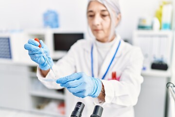 Middle age grey-haired woman wearing scientist uniform using pipette at laboratory