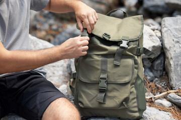 A young man prepares for a hike and packs a large green tactical backpack with pockets - obrazy, fototapety, plakaty