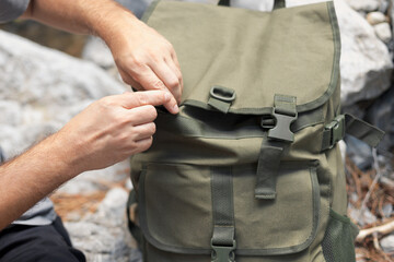 Close-up of a man's hand opening a large khaki hiking backpack at a camping halt