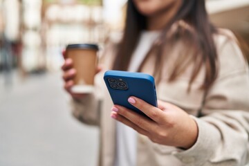 Young hispanic woman using smartphone drinking coffee at street
