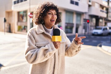 Young beautiful hispanic woman reporter working using microphone at street