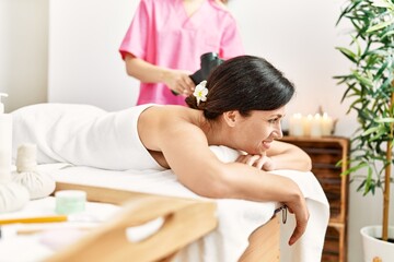 Obraz na płótnie Canvas Middle age hispanic woman smiling confident having back massage using percussion pistol at beauty center