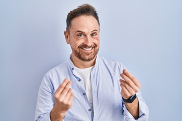 Middle age caucasian man standing over blue background doing money gesture with hands, asking for salary payment, millionaire business