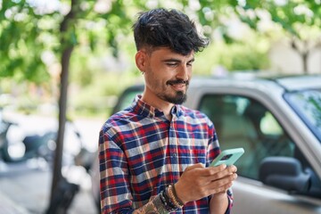 Young hispanic man smiling confident using smartphone at street