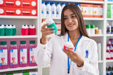 Young beautiful hispanic woman pharmacist holding toothpaste bottles at pharmacy