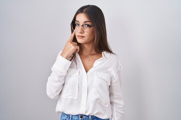 Young brunette woman wearing glasses pointing to the eye watching you gesture, suspicious expression