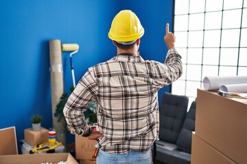 Young hispanic man with beard working at home renovation posing backwards pointing ahead with finger hand