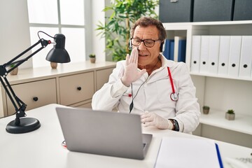 Senior doctor man working on online appointment hand on mouth telling secret rumor, whispering malicious talk conversation