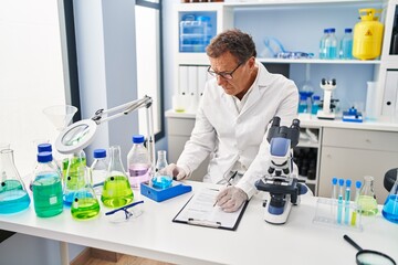 Middle age man wearing scientist uniform measuring test tube writing on clipboard at laboratory