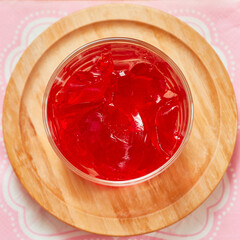 Organic strawberry jello is served in a small glass cup and set on a bamboo plate over a pink napkin