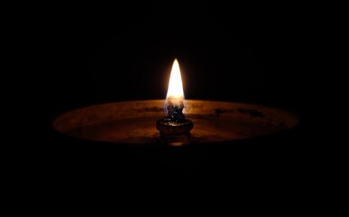 Lit brass oil lamp diya with flame isolated on dark black background with copy space. Old vintage...
