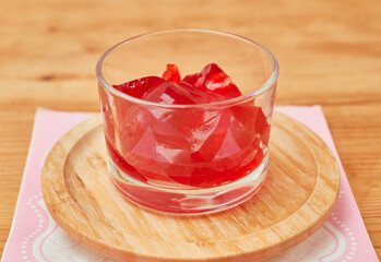 Organic strawberry jello is served in a small glass cup and set on a bamboo plate over a pink napkin - obrazy, fototapety, plakaty