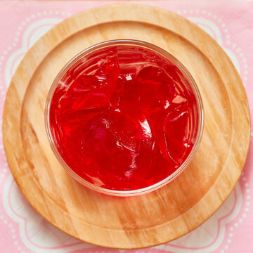 Organic strawberry jello is served in a small glass cup and set on a bamboo plate over a pink napkin
