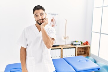 Young handsome man with beard working at pain recovery clinic looking stressed and nervous with hands on mouth biting nails. anxiety problem.