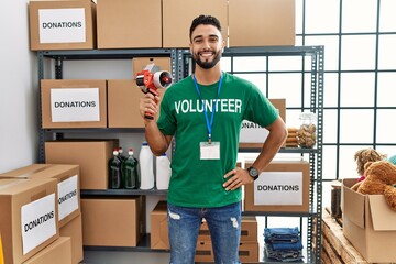 Young arab man wearing volunteer uniform holding packing tape at charity center